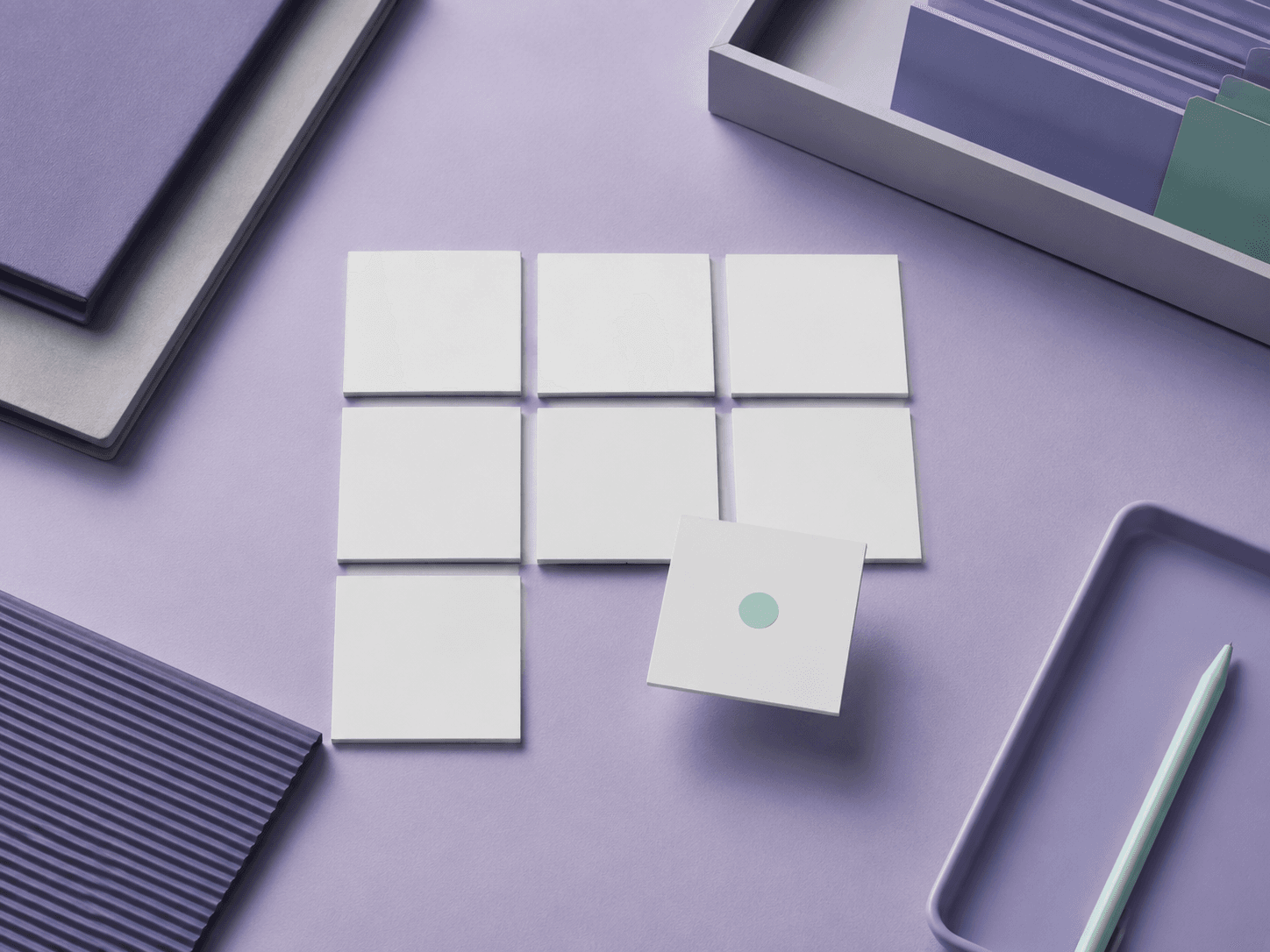 A grid of seven pale square tiles on a violet desk with one tile lifted and marked