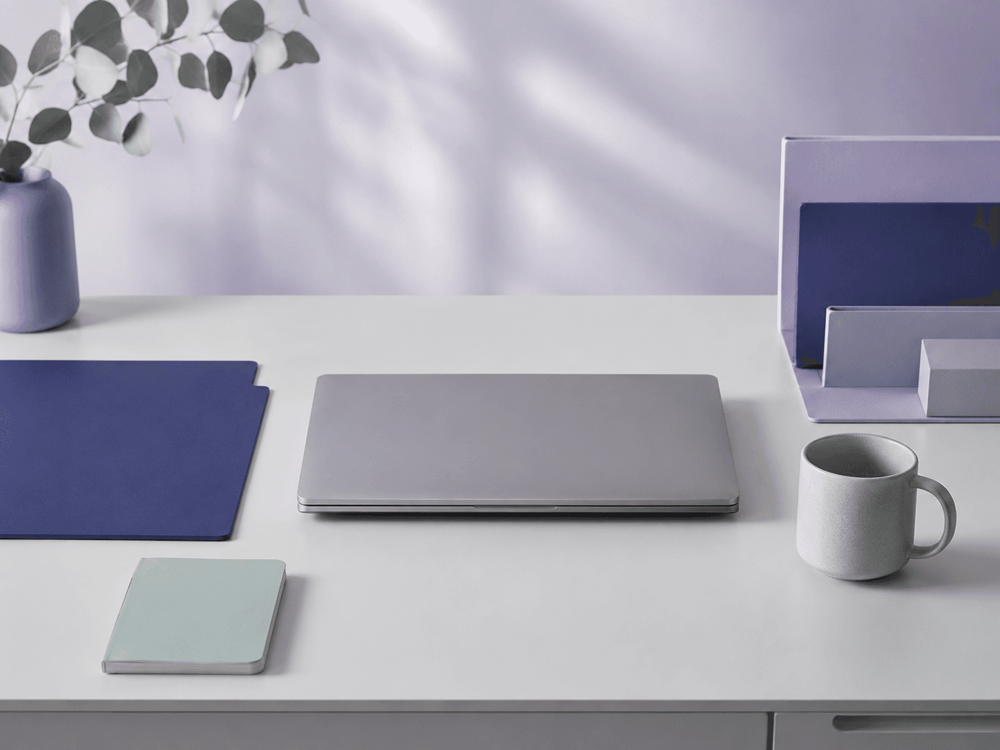 A serene minimal working desk in soft light with a closed laptop, an indigo folder and a mint notebook